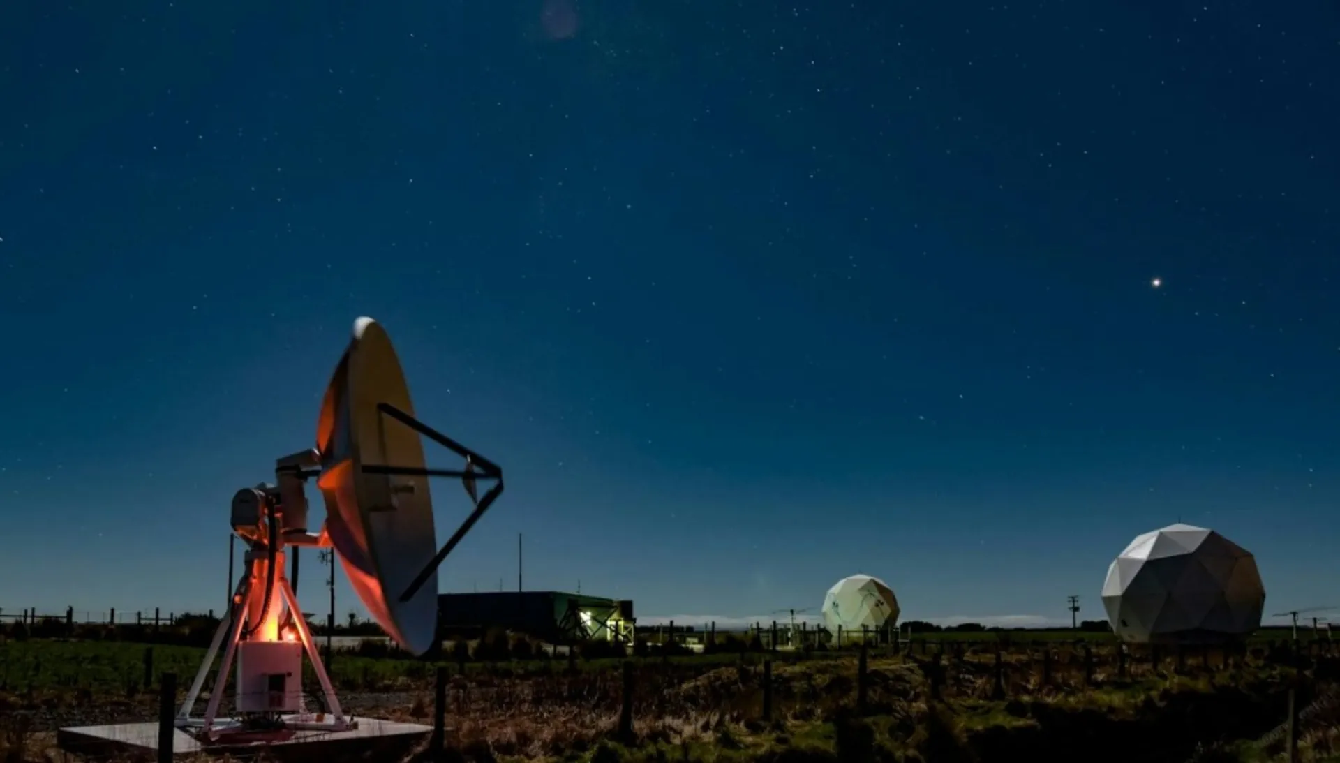 Ground station at dusk with satellite dishes and radomes